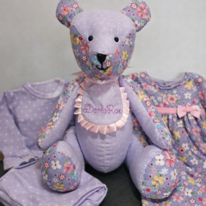 Handmade memory bear created from baby clothing, displayed with the original garments used in its creation, featuring soft lilac floral fabrics.
