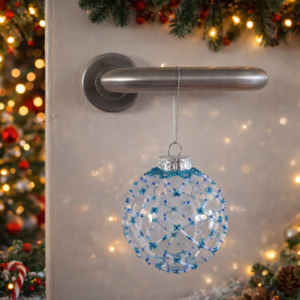 Blue beaded plastic Christmas bauble hanging from a silver door handle with warm festive lights and decorations in the background
