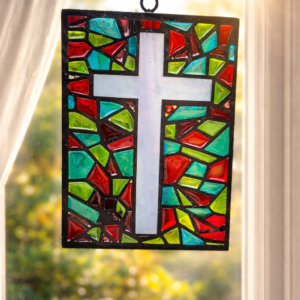 Handmade stained glass effect cross suncatcher with colourful red, green and turquoise resin panels hanging in a sunlit window
