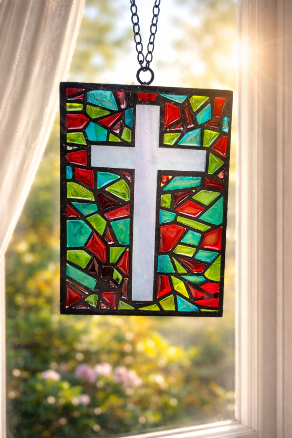 Handmade stained glass effect cross suncatcher with colourful red, green and turquoise resin panels hanging in a sunlit window