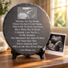 Round slate plaque engraved with an ultrasound baby scan and pregnancy poem displayed on a stand beside a baby scan photo in warm sunlight.