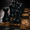 Black resin chess rook, knight and pawn on gold leaf resin chess board under spotlight