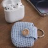 Light blue handmade crocheted AirPods case with AirPods charging case and mobile phone on a wooden table