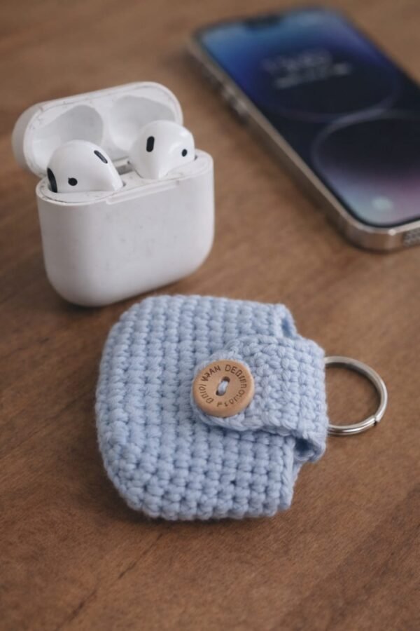 Light blue handmade crocheted AirPods case with AirPods charging case and mobile phone on a wooden table