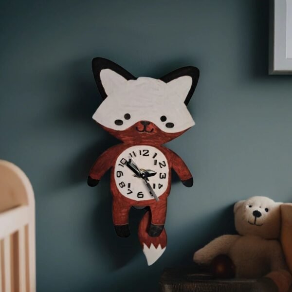 Cute fox-shaped pendulum wall clock with a swinging tail, displayed on a nursery wall beside a teddy bear and cot. The handmade clock features a friendly fox design with a clock face on its tummy, making it ideal for woodland-themed children's bedrooms and playrooms.